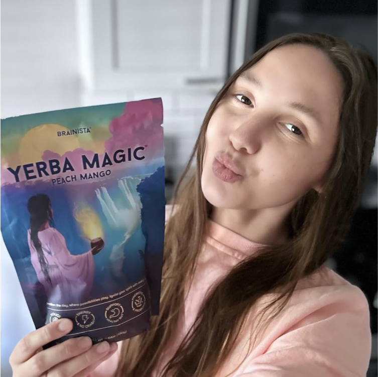 Woman standing in room smiling and holding up a Yerba Magic pouch.