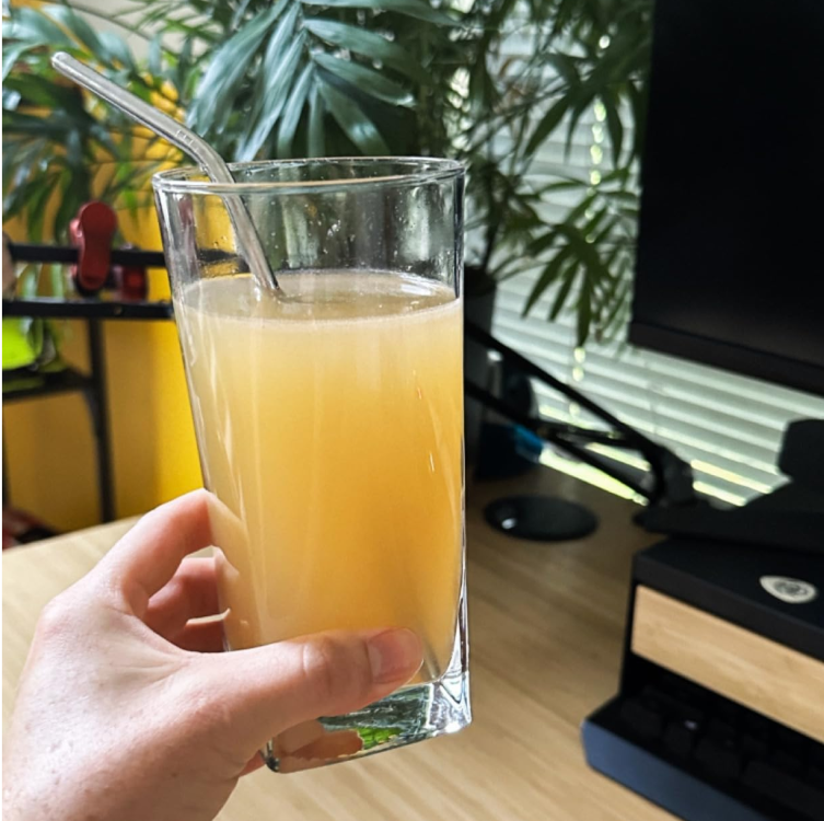 Hand holding a glass of iced Yerba Magic drink with visible froth and vibrant color.
